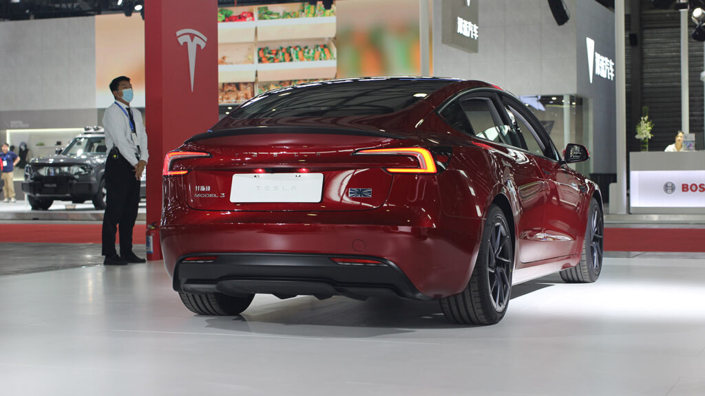 A red Tesla Model 3 displayed at the Shanghai New Energy Vehicle Show in June 2024, viewed from the rear three-quarter angle.