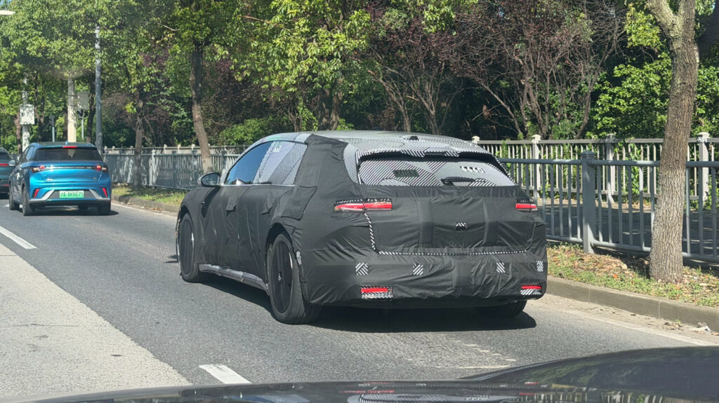 A camouflaged Nio ET5 Touring test vehicle is seen undergoing road testing, viewed from the rear three-quarter angle.