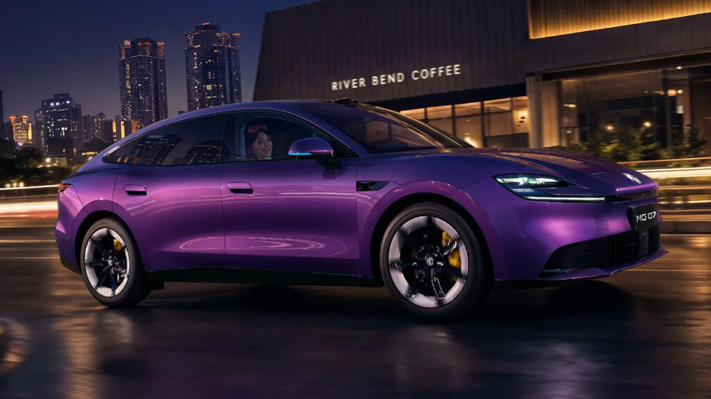 A purple MG 07 sedan driving through a city at night, showing its front three-quarter profile, illuminated headlights and fastback body.