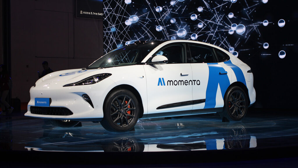 A white Momenta robotaxi with blue graphics and roof-mounted sensors on display at the 2025 Shanghai Auto Show.