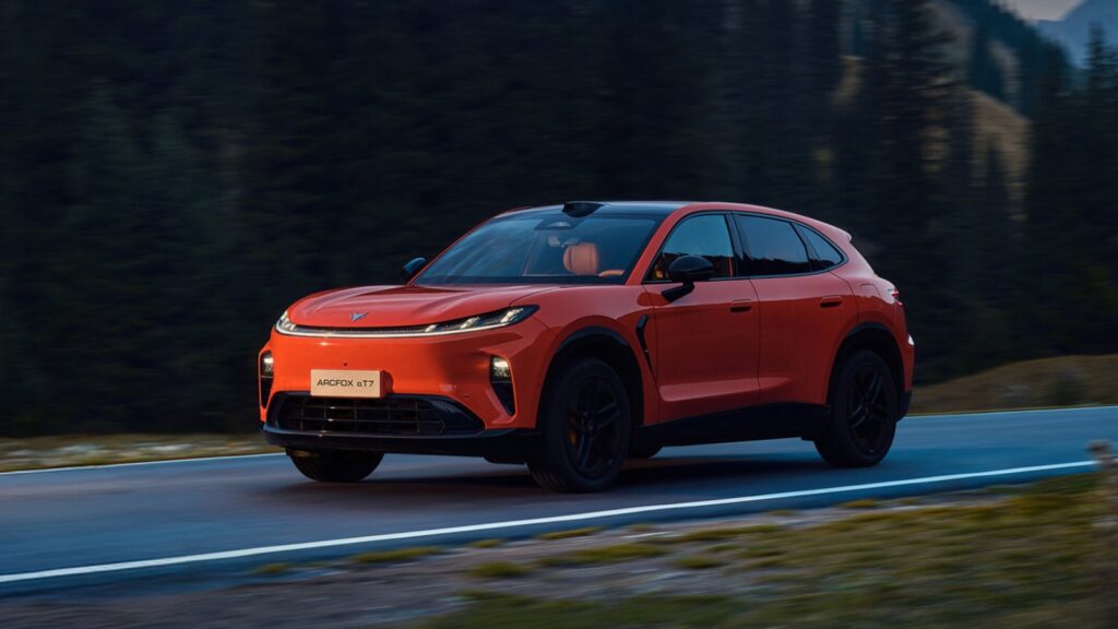 Orange Arcfox Alpha T7 SUV driving along a forest road, viewed from the front three-quarter angle.