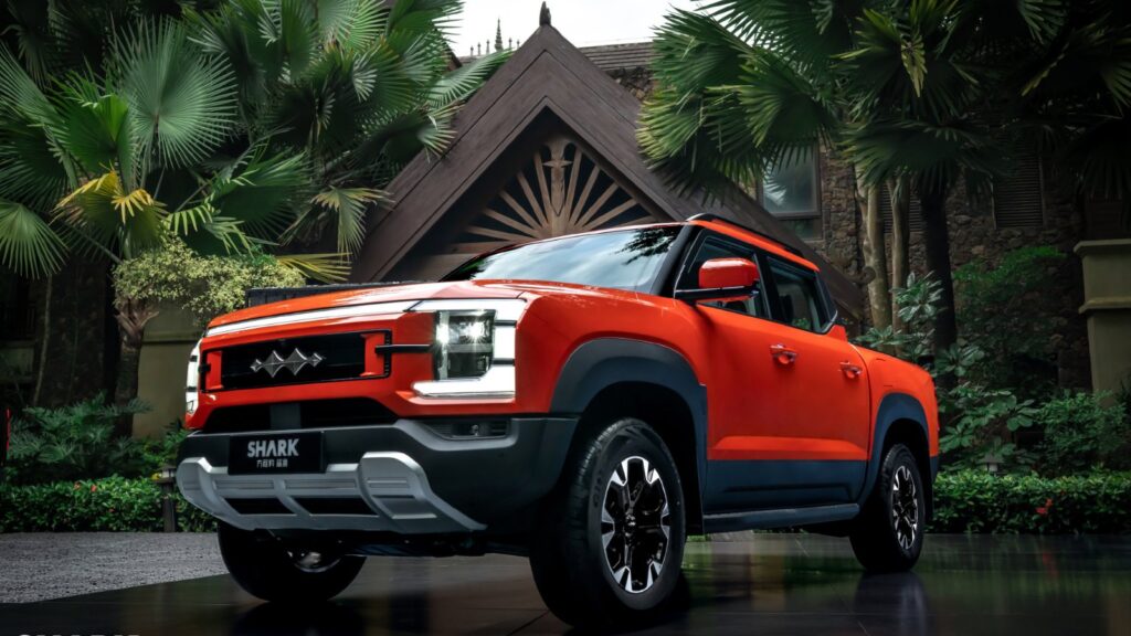 Orange BYD Shark plug-in hybrid pickup with Fang Cheng Bao badging, shown from the front three-quarter angle amid tropical greenery.