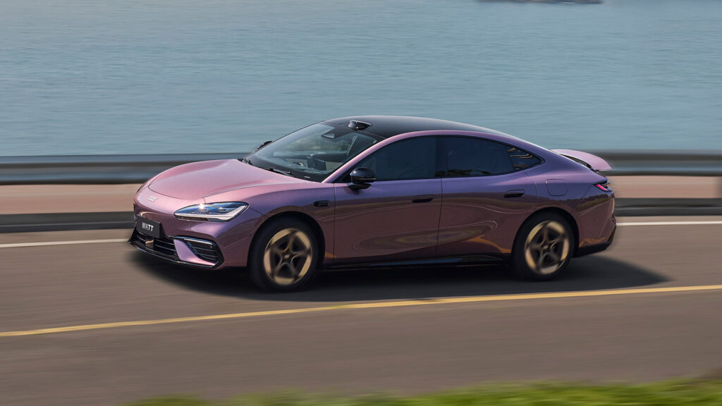 Purple Geely Galaxy TT driving beside the water, showing its fastback profile and raised rear spoiler.