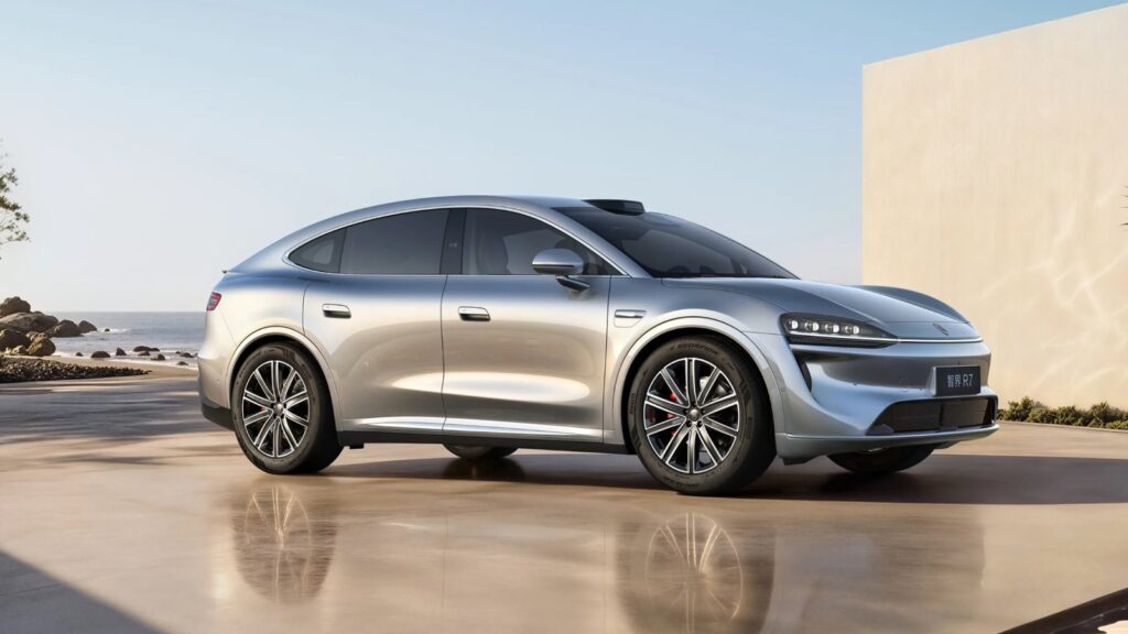 Silver Luxeed R7 coupe SUV shown from a front three-quarter angle beside the sea.
