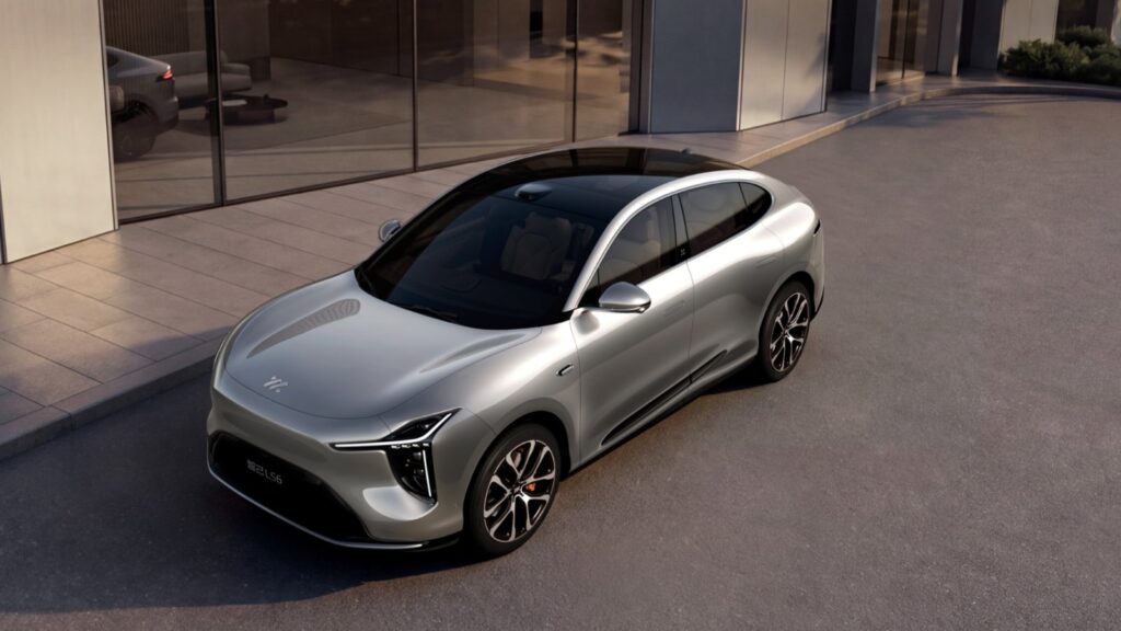 Silver IM Motors LS6 electric SUV viewed from above at a front three-quarter angle outside a modern building.