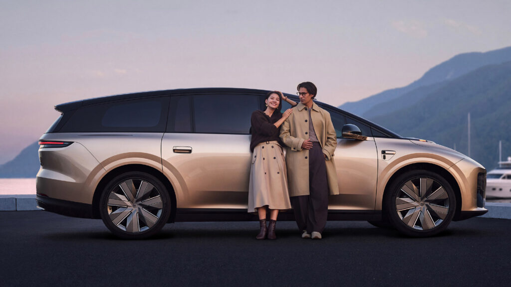 Side view of a gold Li i9 electric SUV with a black roof, with 2 people standing beside it by the waterfront.