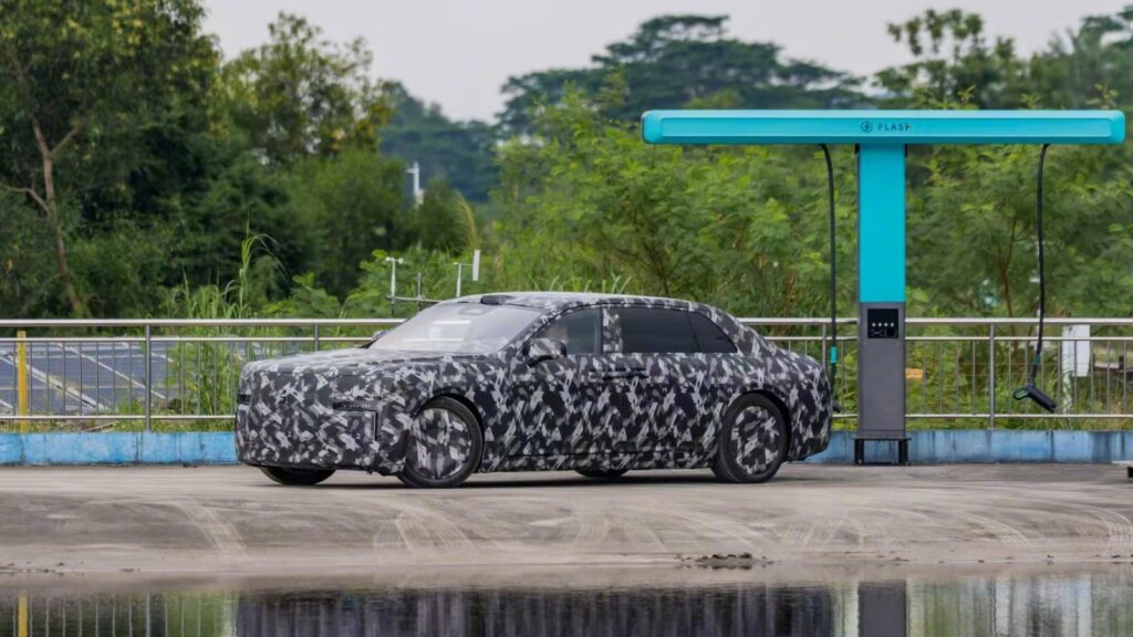 Camouflaged Yangwang executive sedan prototype parked beside a turquoise BYD flash charging station.