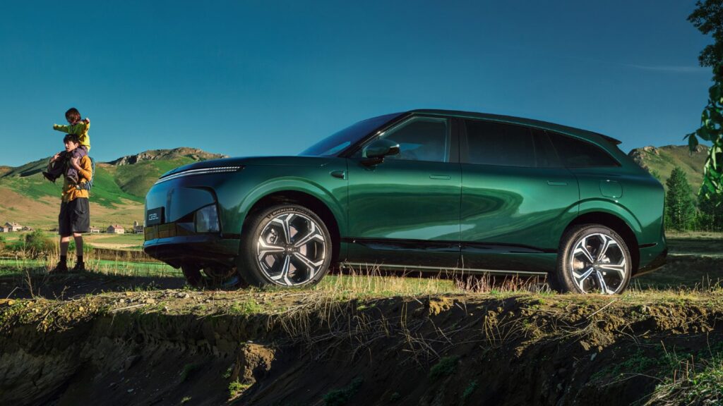 Green Xpeng G9L SUV parked on a grassy bank beside a man carrying a child on his shoulders.