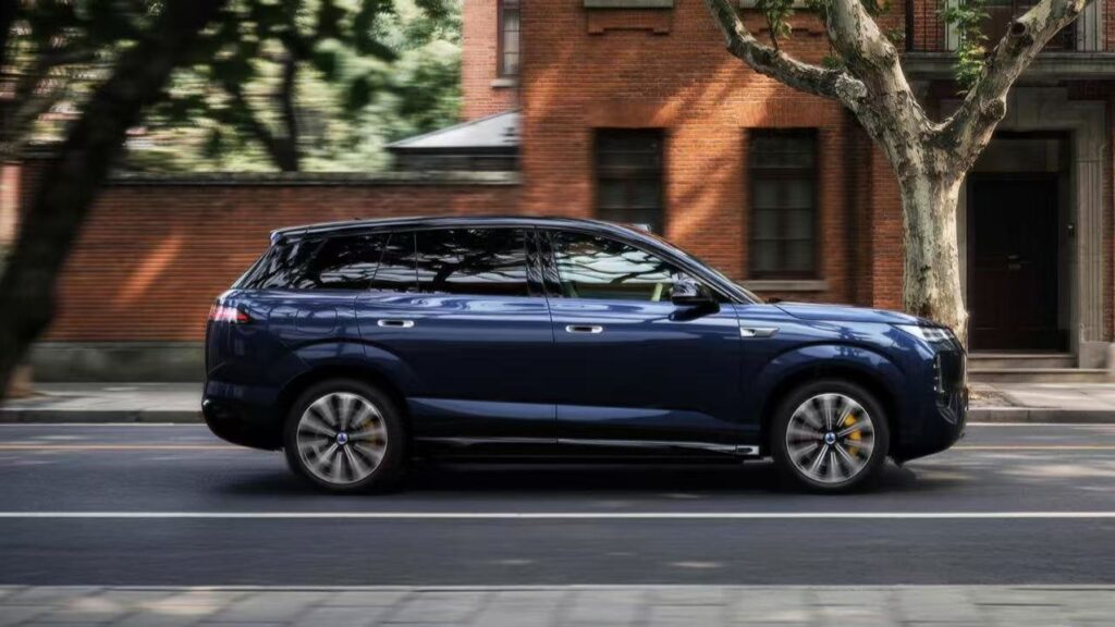 BYD Denza to begin pre-sales of refreshed N8 SUV on October 26 with flash charging Side view of a blue Denza N8 SUV on a tree-lined street beside a brick building.