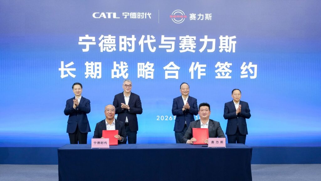 CATL and Seres representatives hold red agreement folders as attendees applaud behind them at a signing ceremony.