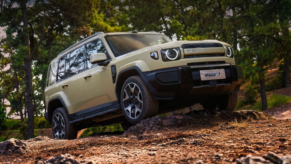 Beige iCar V27 SUV viewed from the front on rocky terrain among trees.