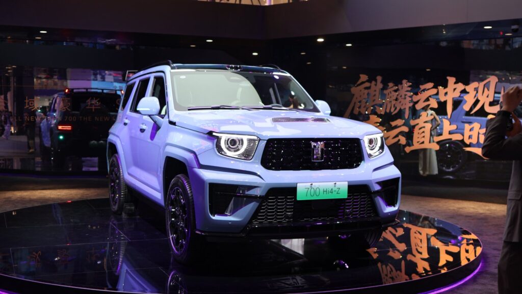 Light blue GWM Tank 700 Hi4-Z SUV displayed on a platform, viewed from the front and side.