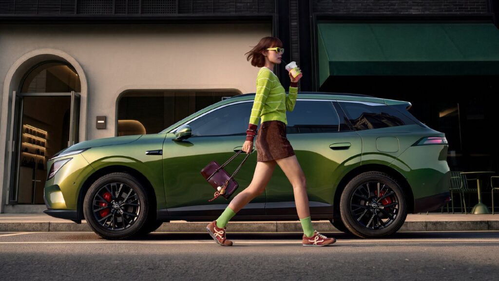 Dongfeng Nissan says NX7 SUV coming soon as N series’ 4th model nears launch Side profile of a green Dongfeng Nissan NX7 SUV parked along a city street, with a woman in a yellow-green sweater walking past it holding a coffee cup.
