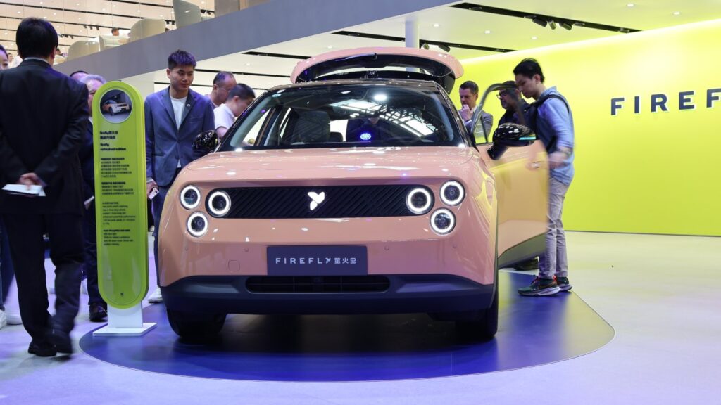 Nio to launch larger 60-kWh battery pack for Firefly on October 23 Front view of a peach-colored Firefly EV with illuminated circular headlights, surrounded by visitors at the 2026 Beijing auto show.