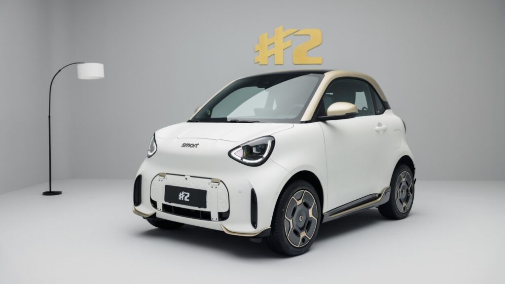 Front three-quarter view of a white Smart #2 Couture Edition with a gold roof, mirrors and exterior trim.