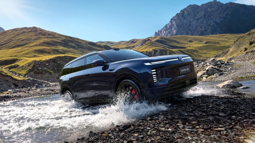 A blue Volkswagen ID. ERA 8X SUV drives through a shallow stream in a mountainous landscape.