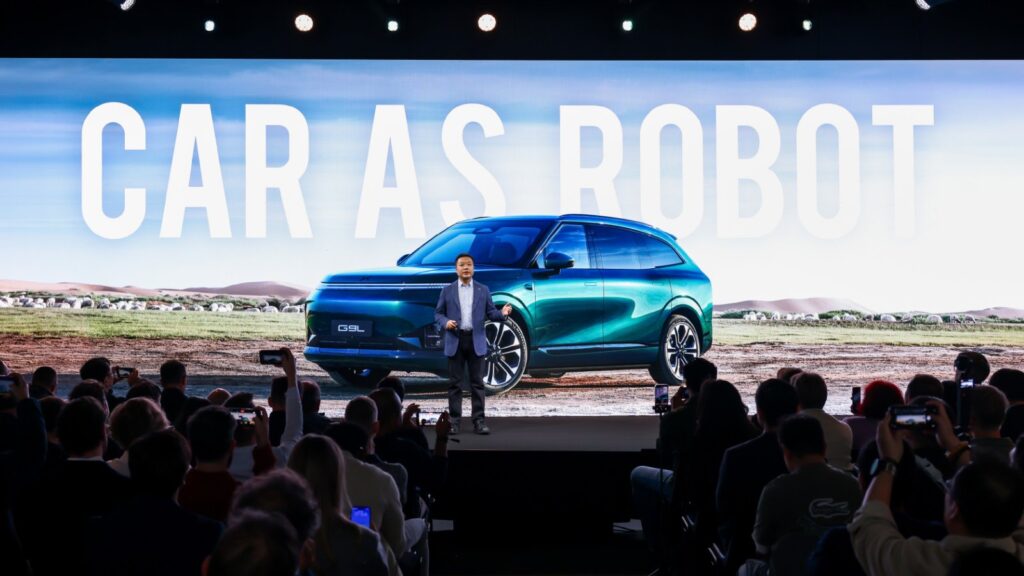 Xpeng chairman and CEO He Xiaopeng speaks onstage in front of a large image of the G9L SUV at the Paris auto show.