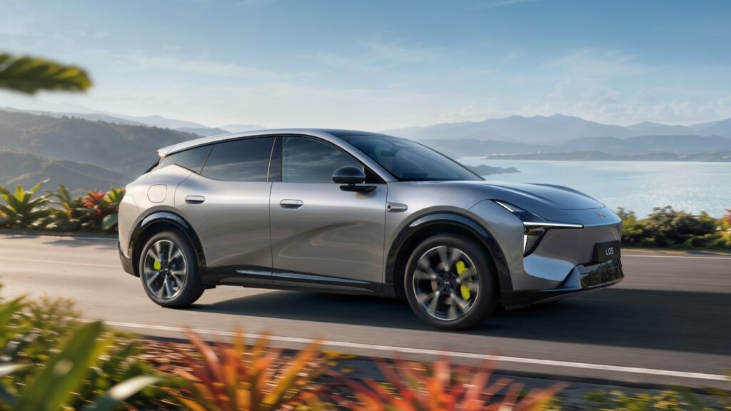 Silver Xpeng Mona L05 SUV driving along a waterfront road with mountains in the background.