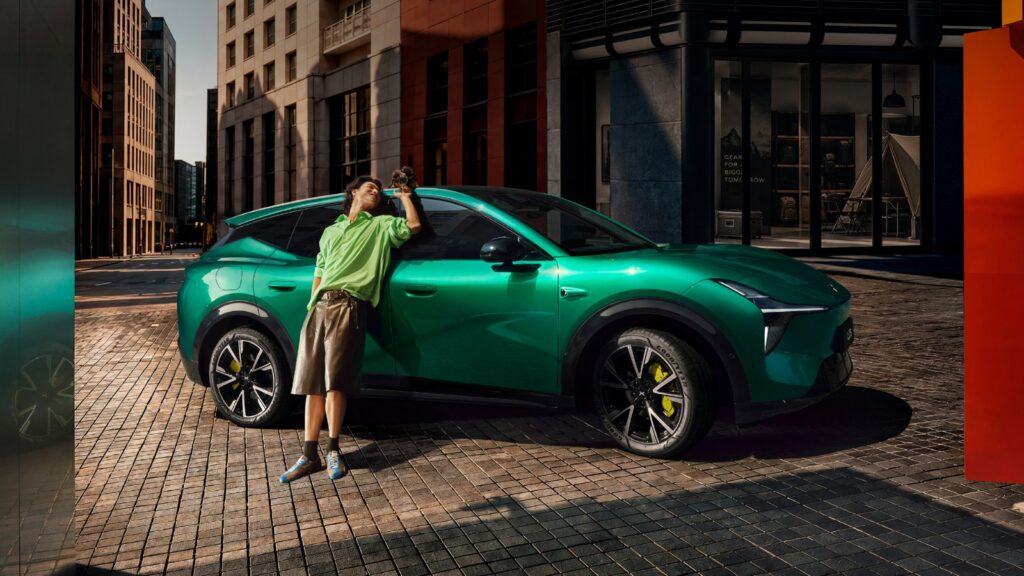 A person holding a camera stands beside a green Xpeng Mona L05 SUV on a city street.