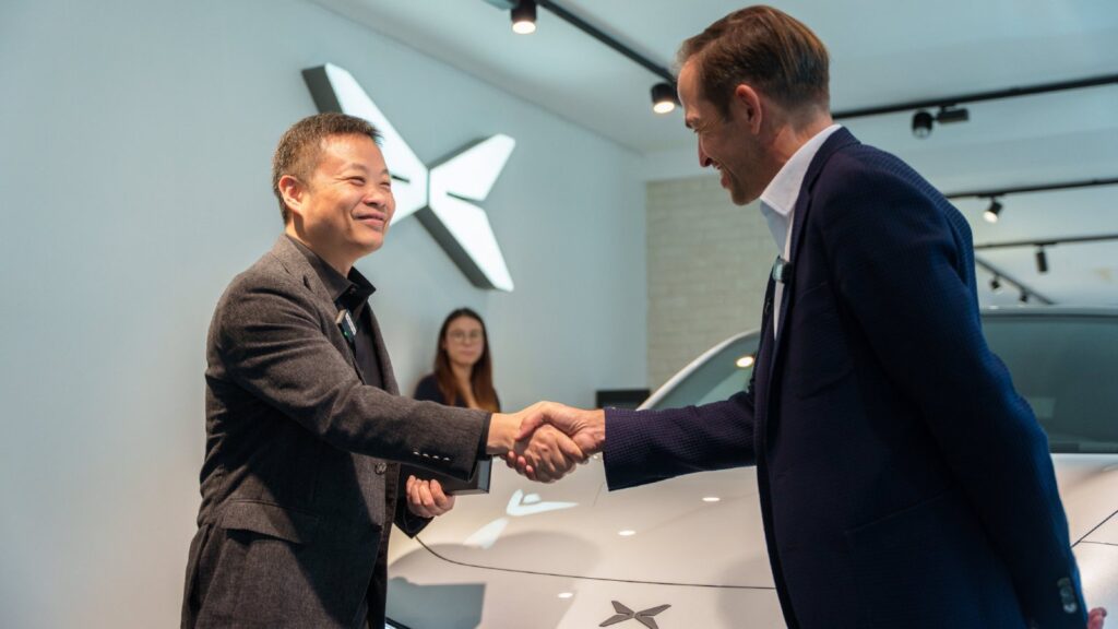 Xpeng chairman and CEO He Xiaopeng, left, shakes hands with a man beside a white Mona L03 in a showroom.
